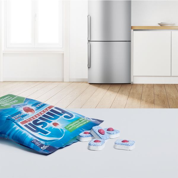 An open package of dishwasher tablets on its side with tablets tumbling out onto the worktop. 