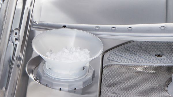 A funnel filled with salt placed in the dishwasher salt tank opening inside a dishwasher.