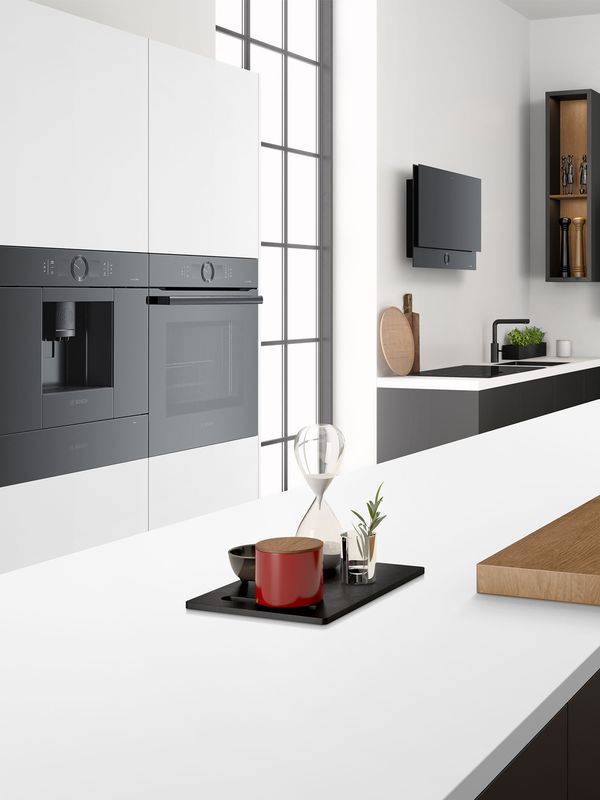 Zwart-witte keuken met zwarte roestvrijstalen apparaten, waaronder een kookplaat met afzuigkap en vaatwasser. Twee open kasten verlichten het werkgedeelte