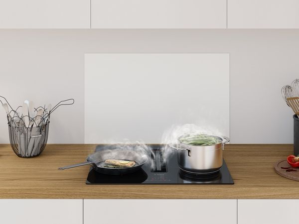Strakke ingebouwde elektrische kookplaat van 60 centimeter in zwart glas en een roestvrijstalen pan in de hoek