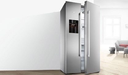 Sølvfarget frittstående Side-by-Side Bosch-kjøleskap på et moderne hvitt kjøkken. Døren er åpen og man kan se matvarer. 