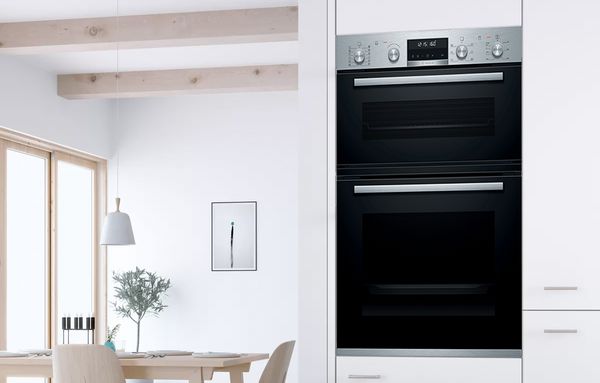 Bosch dubultā cepeškrāsns, kas iebūvēta sienā modernā, baltā virtuvē. 