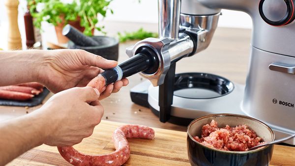 Una macchina da cucina OptiMUM Serie 8 che prepara salsicce con l'accessorio HuntingAdventure.