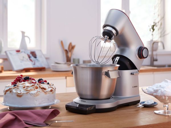 Bosch kuhinjski robot sa metlicom za mućenje pored torte i umućenog šlaga.