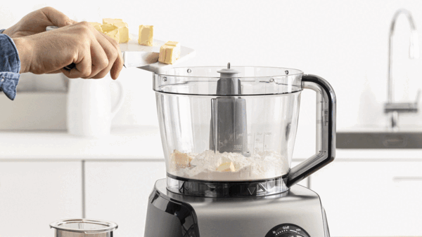 Une personne qui ajoute du beurre coupé en dés dans le robot multifonction pour faire une pâte feuilletée.