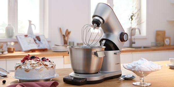 Dans une cuisine, on peut voir, entre autres, un gâteau tout juste sorti du four et un robot de pâtissier Bosch avec un grand bol mélangeur.