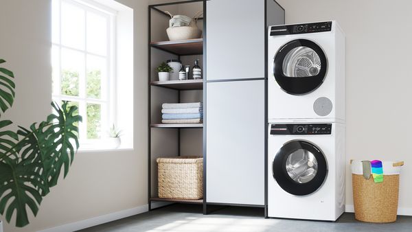 En tørretumbler stablet på en vaskemaskine i et badeværelse og påklædningsområde.