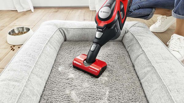 Red Unlimited ProAnimal vacuum cleaning a dog's bed.