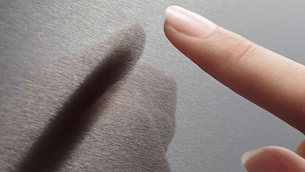 A finger touching the surface of a stainless steel Bosch fridge with Anti Fingerprint.