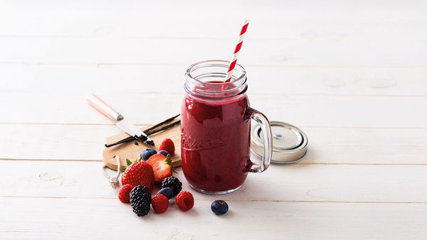 Κόκκινο smoothie σε ποτήρι μαζί με κόκκινα φρούτα και λοβό βανίλιας πάνω σε τραπέζι.
