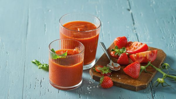 Due bicchieri di frullato rosso sistemati su un tavolo con alcune fragole e pomodori.