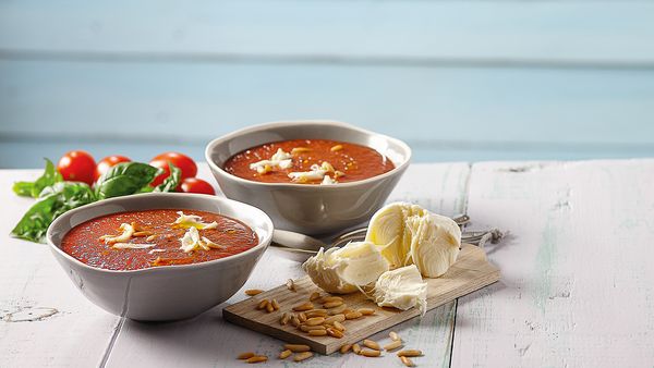 Zwei kleine Schüsseln mit Tomatensuppe, angerichtet mit Knoblauchzehen, Basilikumblättern und Tomaten, auf einem Tisch.