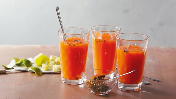 Tres batidos de naranja en vasos organizados juntos, con rodajas de manzana y lima sobre una mesa.
