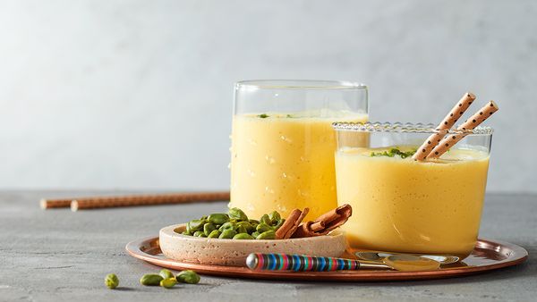 Dos cremas de color amarillo a base de duraznos servidos en vasos dispuestos juntos con un bol pequeño de pistachos.