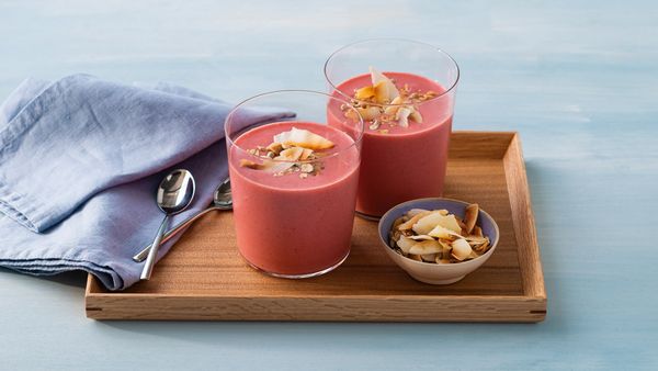 Dois batidos avermelhados servidos em copos num tabuleiro decorado com uma pequena tigela de granola e flocos de coco.