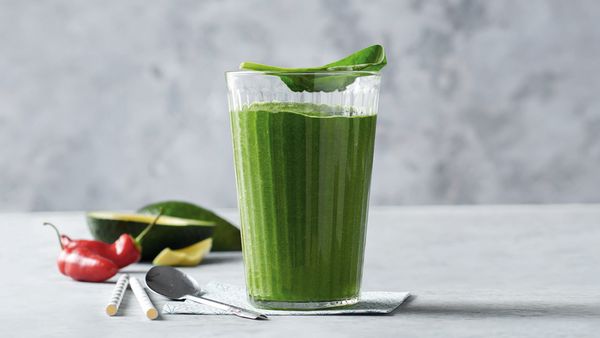 Grüner Smoothie in einem Glas, angerichtet mit einer Avocadohälfte und einer Chilischote.