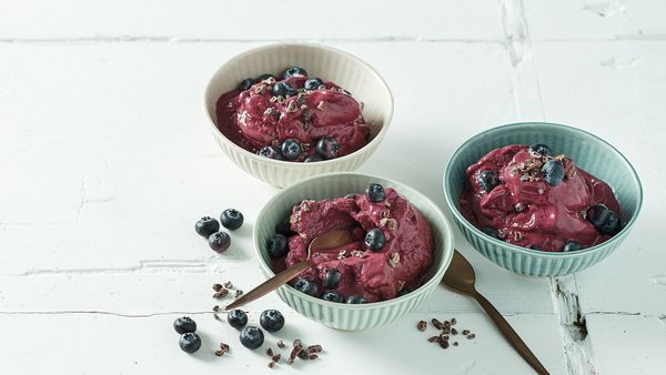 Três tigelas cheias de creme gelado, pulvilhadas com mirtilos.