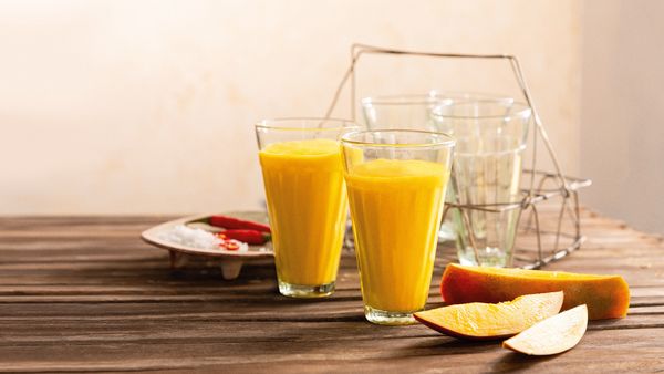 Two yellow smoothies made from mangos filled in glasses and arranged together with mango slices.