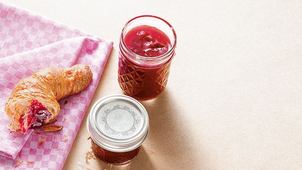 Ein mit Himbeermarmelade gefülltes Glas, angerichtet mit einem Croissant.