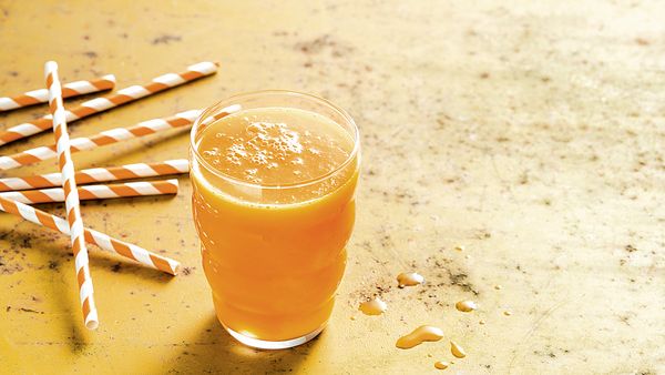 Zumo amarillo de varias frutas y verduras envasado en un vaso.