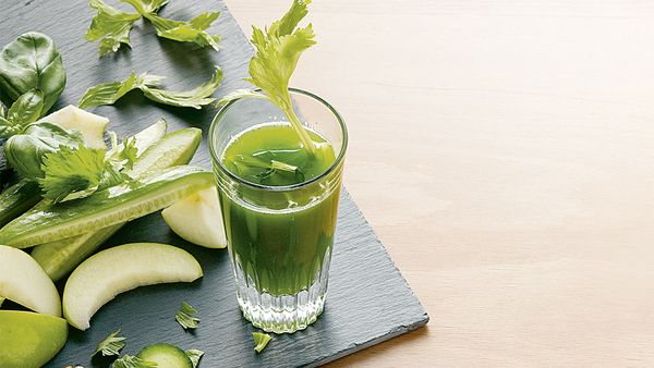 Grüner Saft in ein Glas gefüllt, angerichtet mit Apfelscheiben und Gurken- und Selleriestücken.
