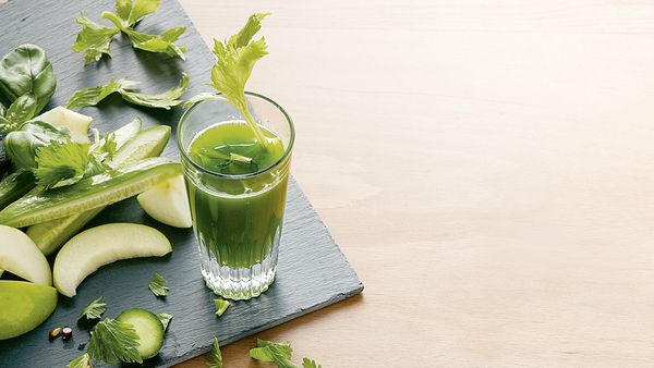 Grüner Saft in ein Glas gefüllt, angerichtet mit Apfelscheiben und Gurken- und Selleriestücken.