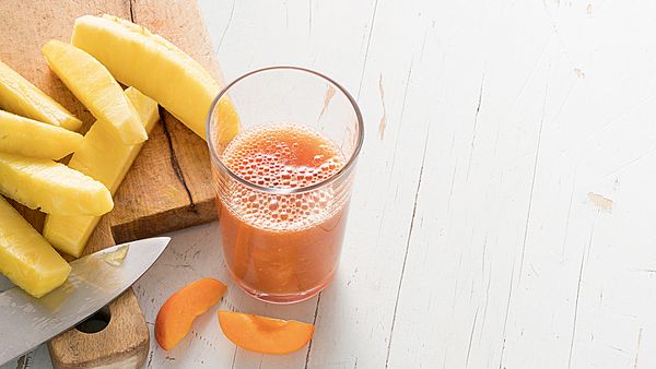 Jus jaune versé dans un verre et disposé avec des tranches d'ananas et d'abricots.