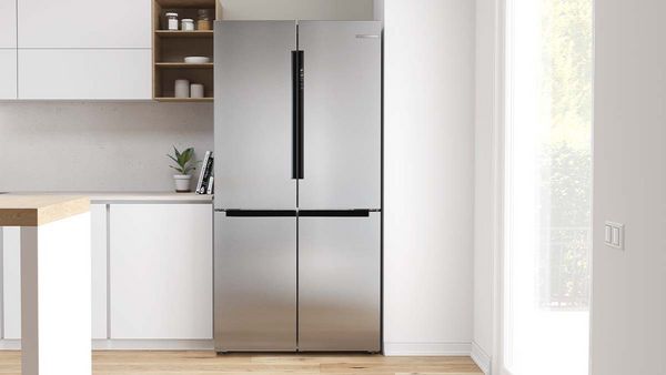 Køleskab med franske døre med sorte håndtag ved siden af et vindue i et åbent køkken.