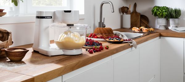 Auf einer Küchenarbeitsplatte befinden sich verschiedene Koch- und Backzutaten sowie eine rote Bosch Küchenmaschine.