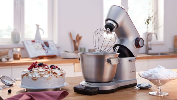 Robot de cocina Bosch con un batidor al lado de un pastel y crema batida.