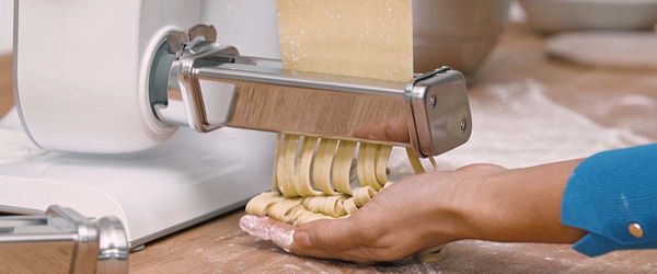 Close-up of stand mixer with PastaPassion attachment, with pasta being fed through to make tagliatelle.