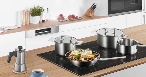 Different induction pots and pans on a Bosch induction hob in a white kitchen.