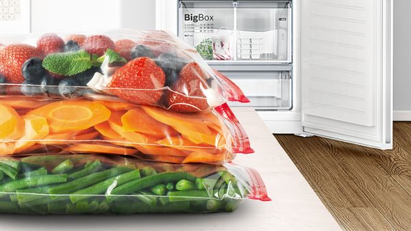 Frutta e verdura in sacchetti per il congelamento. Congelatore aperto sullo sfondo.