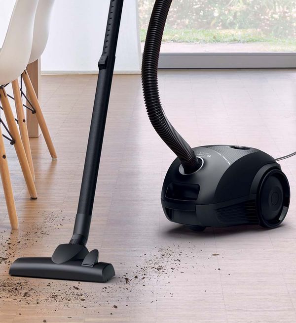 A bagged cylinder vacuum sucks up visible dirt on the floor.