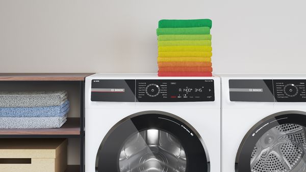 En stabel kulørt vasketøj, der er lagt sammen på en vaskemaskine.