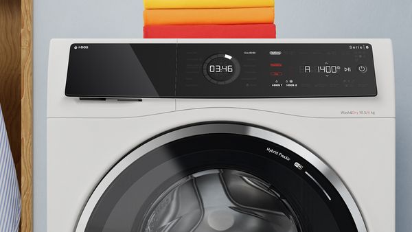 Nærbilde av pent brettede håndklær i samme farge som energimerkingen er stablet på et kombinert vask og tørk-apparat. 