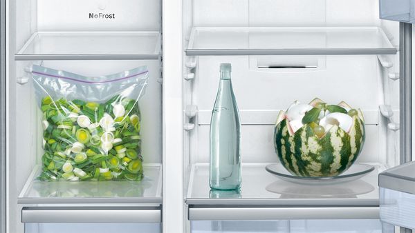 Des poireaux congelés, une grande bouteille d'eau et une grosse pastèque dans un réfrigérateur.