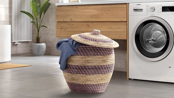 Bosch-Frontlader-Waschmaschine in einem modernen Badezimmer mit geflochtenem Wäschebehälter mit Deckel 