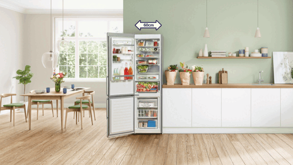 Atvērta Bosch lielā ledusskapja saldētava, kas piepildīta ar svaigām pārtikas precēm, piemēram, cepamplāti, lielu arbūzu un pudelēm.