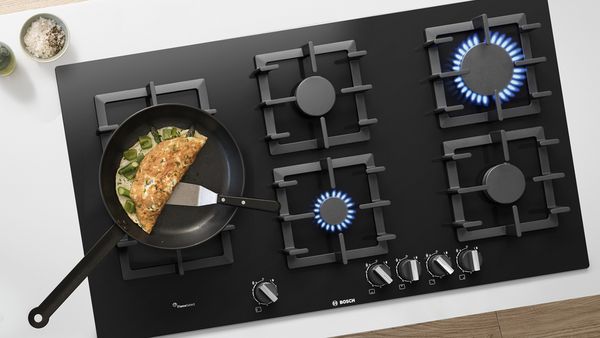 An omelette cooking on top of a gas hob with 5 burners.