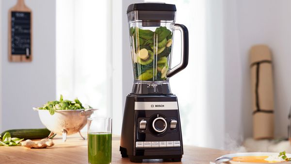 Bosch high performance blender VitaBoost with fruits and vegetables and a smoothie glas on a kitchen shelf.