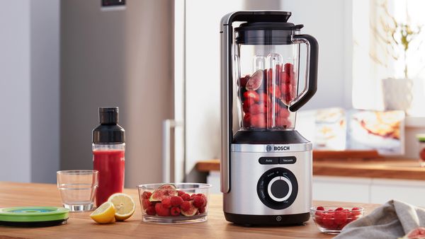 Blender próżniowy VitaPower Serie 8 marki Bosch stojący na półce kuchennej z owocami i pojemnikiem na wynos w tle.