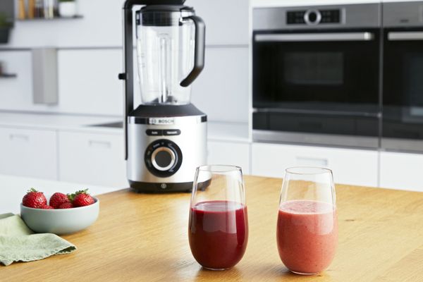 Zwei rote Smoothies stehen auf einer Küchenabstellfläche, mit dem Bosch Vakuum-Mixer VitaPower Serie 8 im Hintergrund.