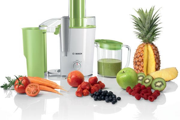 Центробежная соковыжималка Bosch зеленого цвета с аксессуарами и различными фруктами и овощами рядом с ней.