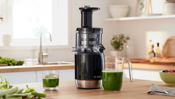 Ο αποχυμωτής αργής εκχύμωσης VitaJuice της Bosch γεμάτος πράσινο χυμό στον πάγκο μιας κουζίνας.