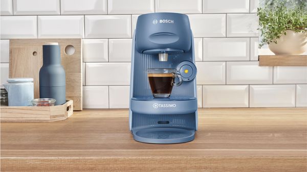Die Kaffeemaschine TASSIMO FINESSE auf einer Küchenarbeitsplatte mit einer gefüllten Espressotasse.
