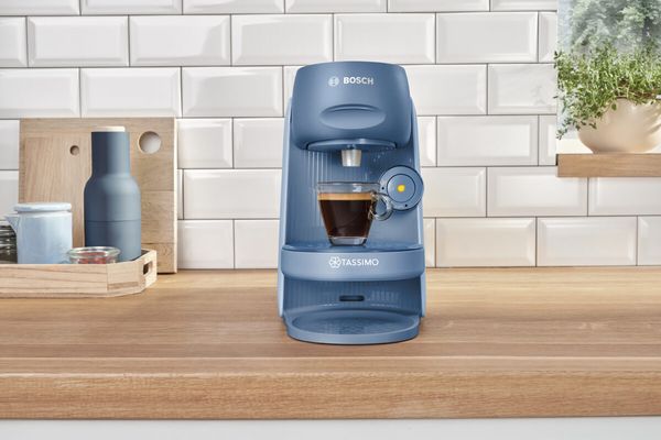 Die Kaffeemaschine TASSIMO FINESSE auf einer Küchenarbeitsplatte mit einer gefüllten Espressotasse.