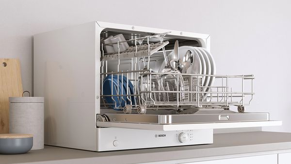 A countertop dishwasher with an open door and a full rack on a kitchen worktop.