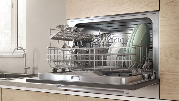 A small built-in dishwasher with an open door and a full rack.