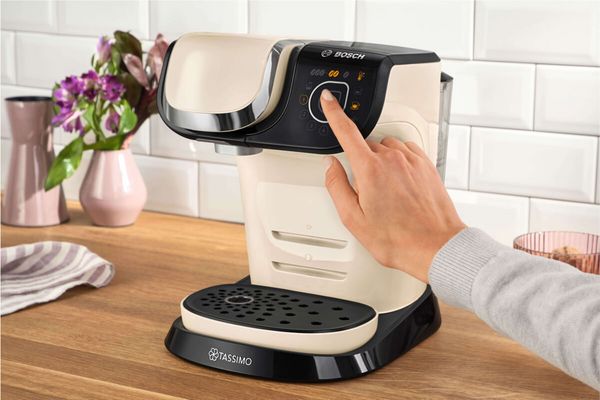 Alt text: A person clicks the start button on the TASSIMO coffee machine MYWAY 2.